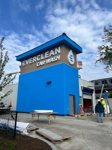 Blue car-wash building under construction, with workers nearby and a tall sign reading 'EverClean Car Wash' under a bright sky